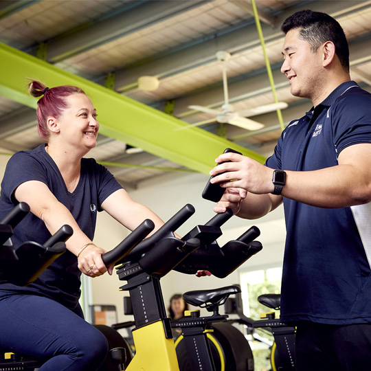  Personal training client on spin bike with AKAC personal trainer instructing